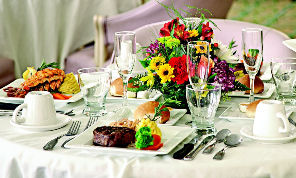 An elegantly set dining table with a steak dish and colorful flower centerpiece.
