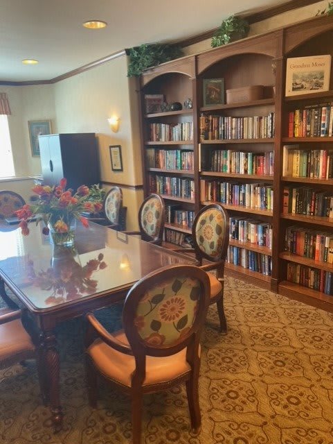 A cozy library with bookshelves lining the walls, featuring a wooden table and ornate chairs.