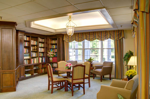 A cozy reading room with bookshelves, a table, and chairs near large windows.