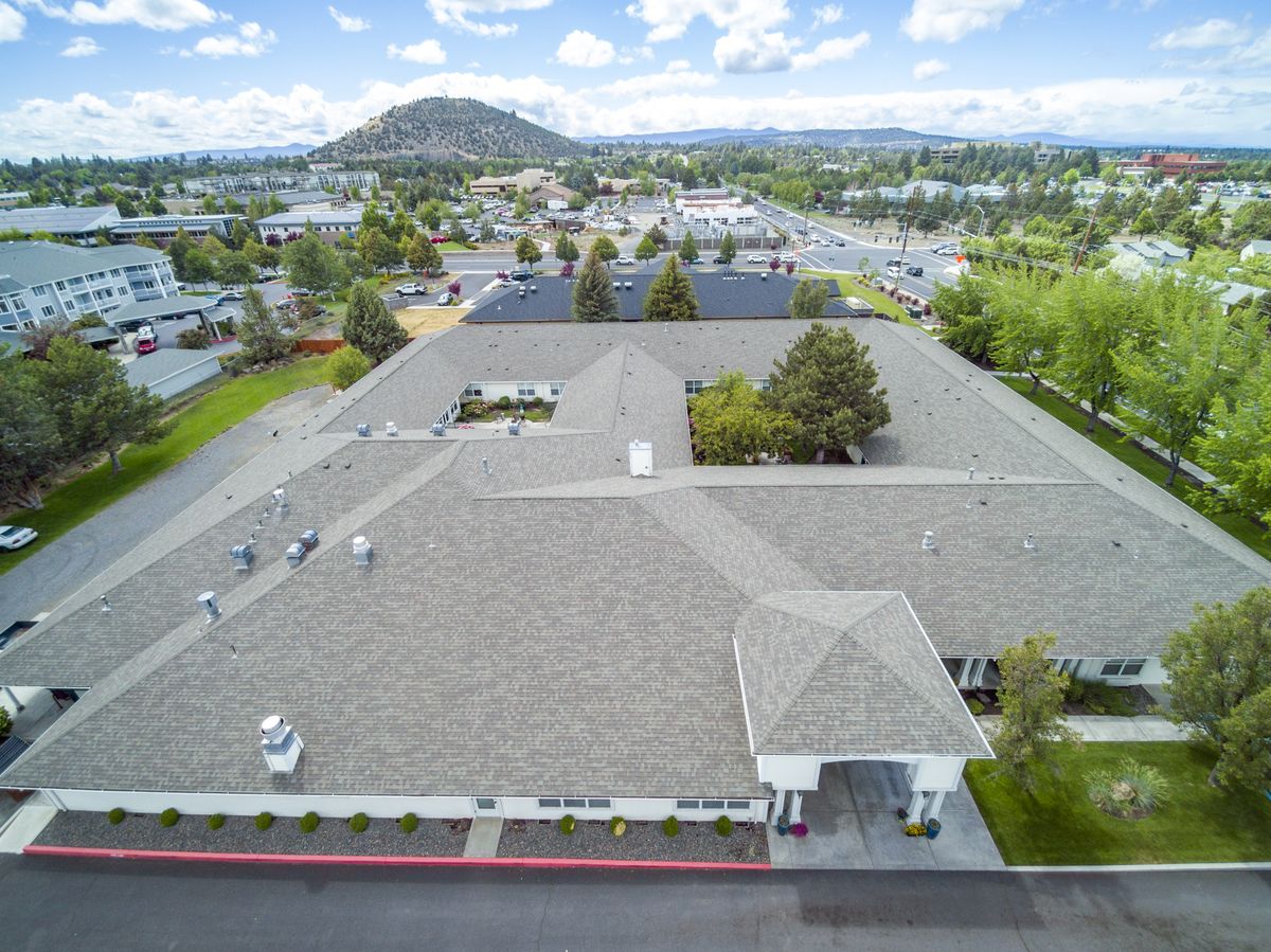 An aerial view of a large building surrounded by greenery and suburban landscape under a blue sky.