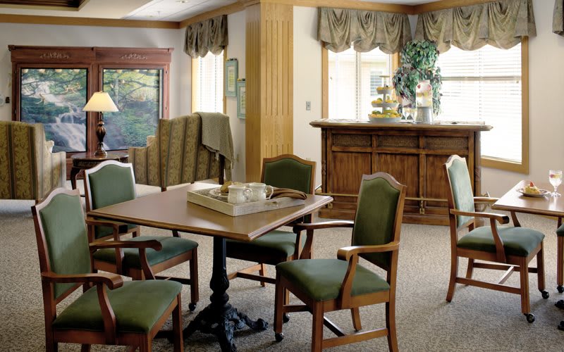 A cozy dining area with a wooden table, green upholstered chairs, and large windows letting in natural light.