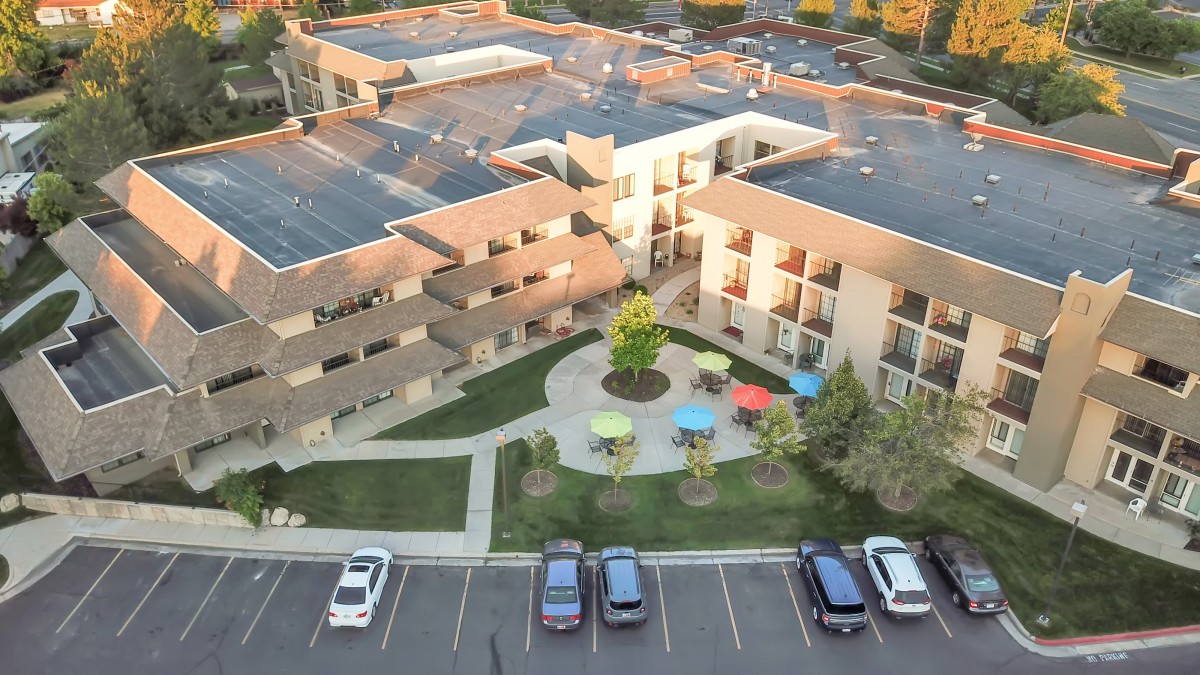 Aerial view of an apartment complex featuring a landscaped courtyard with colorful patio umbrellas and adjacent parking spaces.