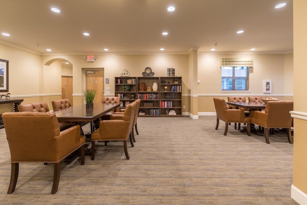 A cozy library space with tables, chairs, and bookshelves under warm lighting.