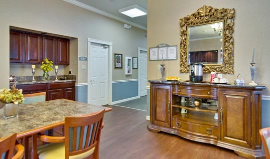 A cozy interior space featuring a wooden cabinet with a large ornate mirror, a dining table with chairs, and a hallway leading to other rooms.