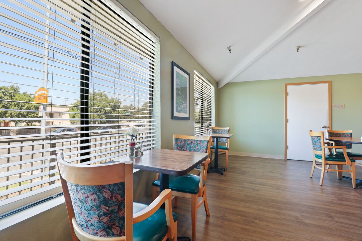 A bright and cozy cafe interior with tables and chairs next to large windows.
