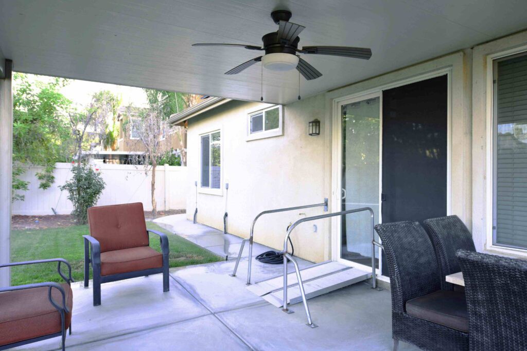 A covered patio featuring a ceiling fan, chairs, and a ramp leading to a sliding glass door.
