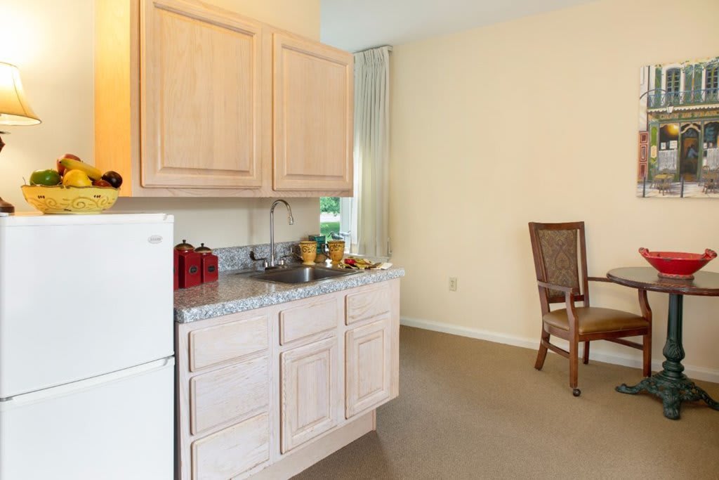 A small kitchen area with light wood cabinets, a sink, and a dining table with chairs.
