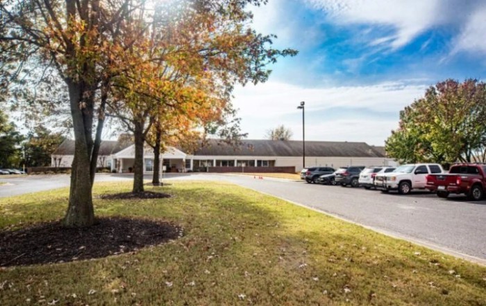A wide view of a building with an adjacent parking lot and trees with autumn foliage under a blue sky.