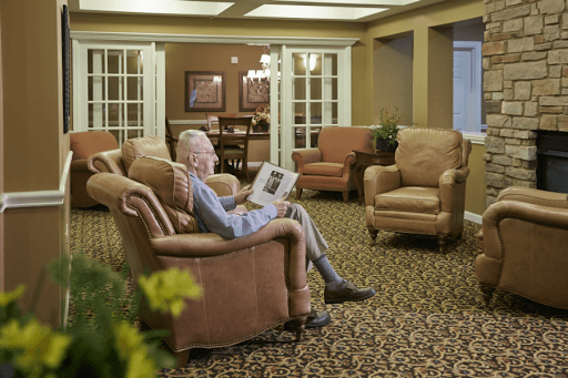 An elderly person sitting comfortably in an armchair while reading a newspaper in a cozy living room.