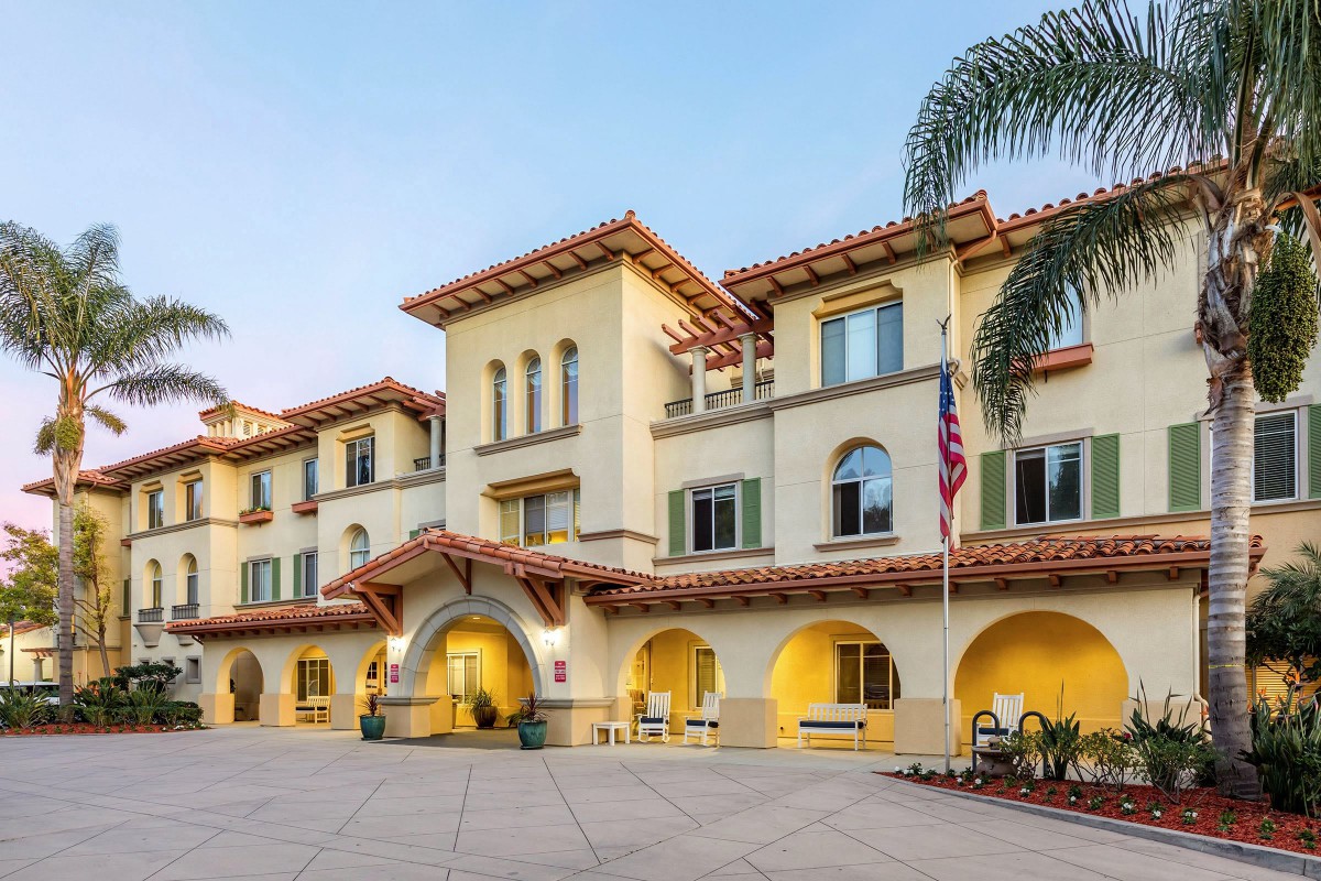 A Mediterranean-style building with large arches and palm trees at the entrance.