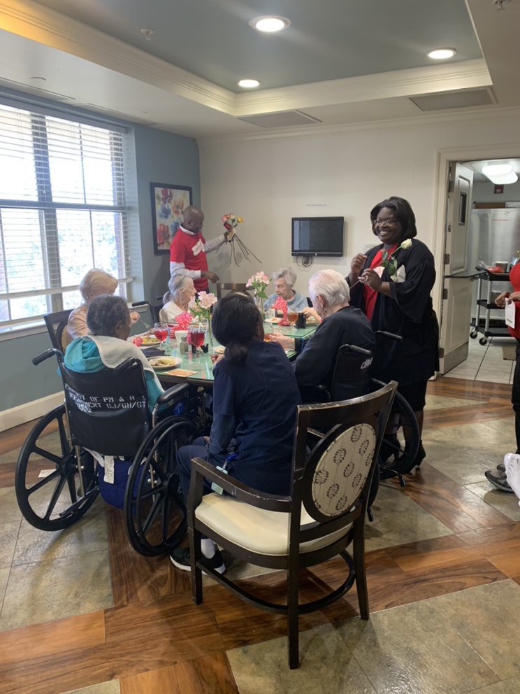 A group of seniors and caregivers gathered around a table at a nursing home.