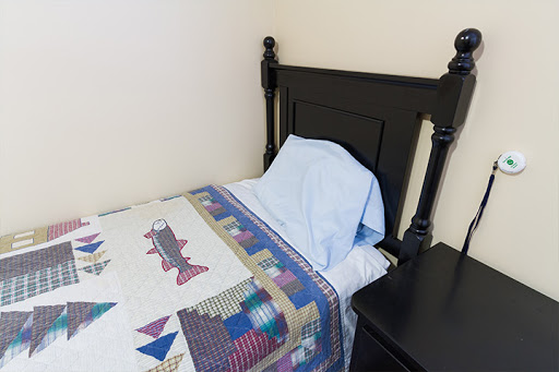 A neatly made bed with a colorful quilt and a light blue pillow.