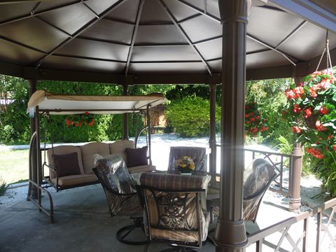 A cozy backyard gazebo with comfortable patio furniture and a swing, surrounded by lush greenery.