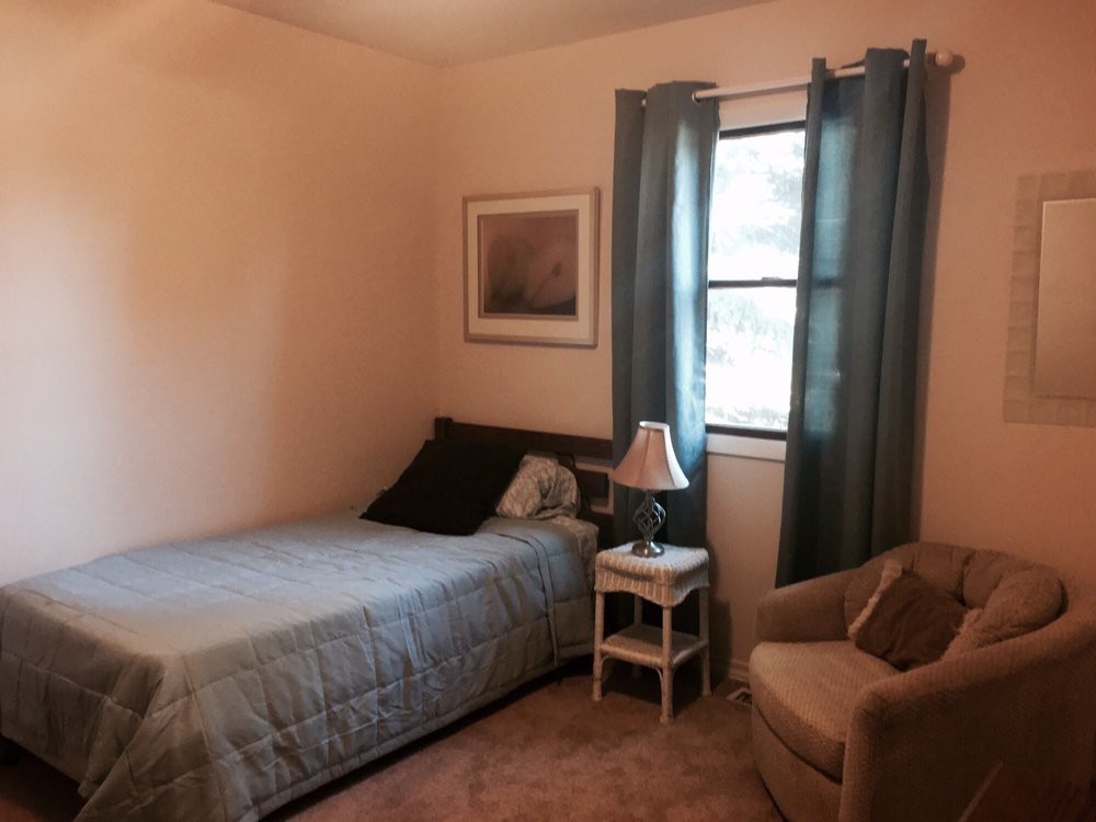 A cozy bedroom with a single bed, nightstand, and an armchair by the window.