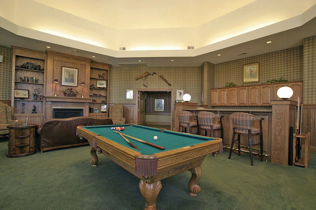 A cozy billiard room featuring a pool table, bar seating, and traditional wooden decor.