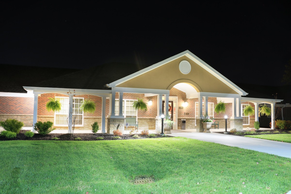 A brightly lit house at night with a well-maintained lawn.