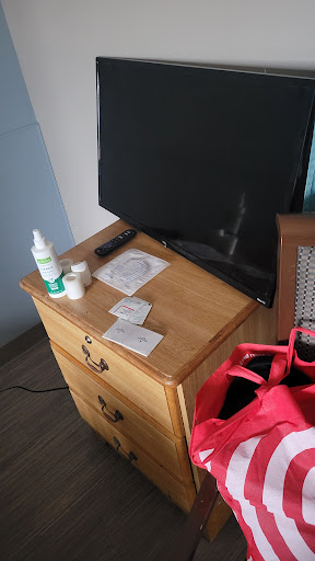 A wooden nightstand in a bedroom with a television, healthcare products, and a pink bag.