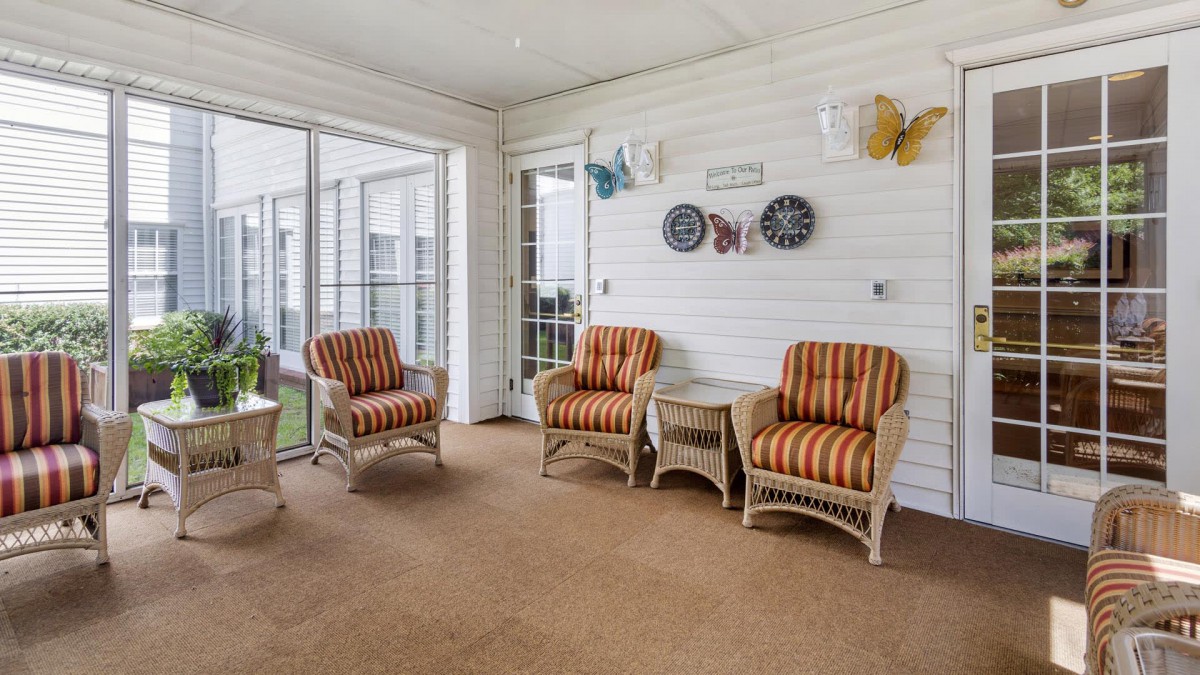 A cozy sunroom featuring wicker furniture with striped cushions, decorative wall art, and ample natural light through glass doors.