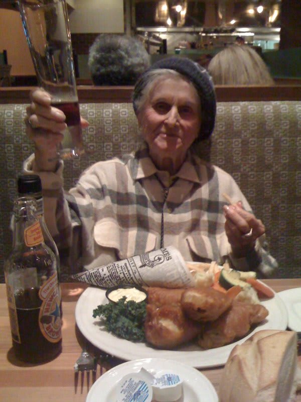 An elderly woman enjoying a meal at a restaurant, raising a glass in celebration.