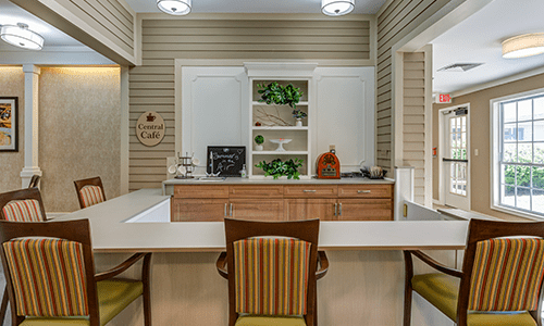 A cozy kitchen interior with a central counter and chairs, featuring decorative shelves.