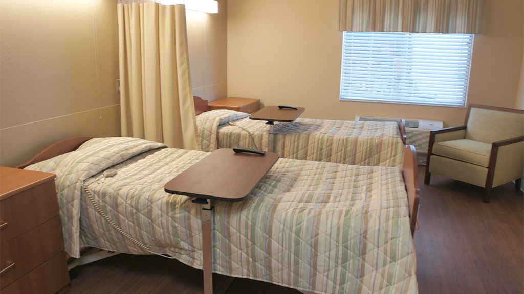 A hospital room with two beds, each equipped with a movable overbed table.