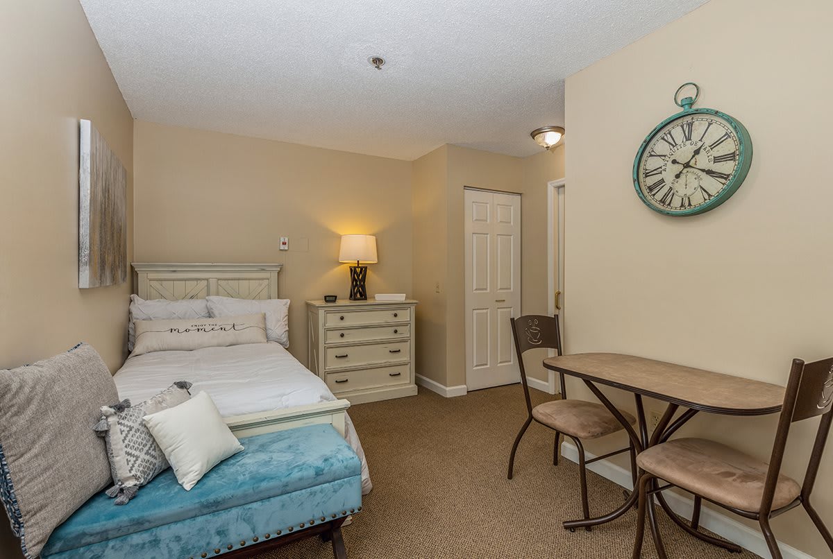 Cozy bedroom with a bed, table and chairs, featuring a decorative wall clock.