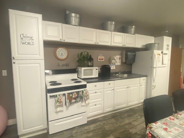A cozy kitchen with white cabinets and various appliances, including a stove, microwave, and refrigerator.