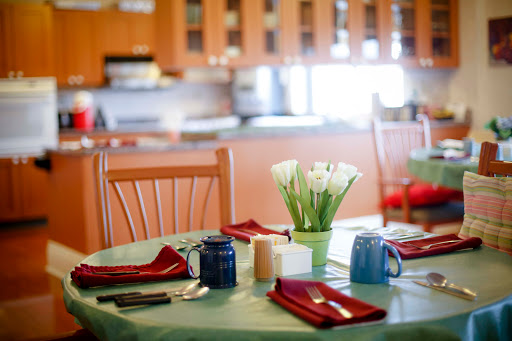 A beautifully set dining table with flowers, utensils, and colorful coffee cups in a cozy kitchen.