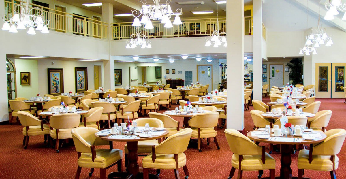 A spacious dining area with multiple tables and chairs, elegantly lit by chandeliers.