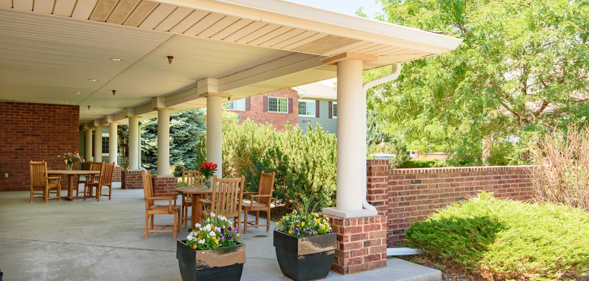 A cozy patio with wooden furniture surrounded by lush greenery and brick accents.
