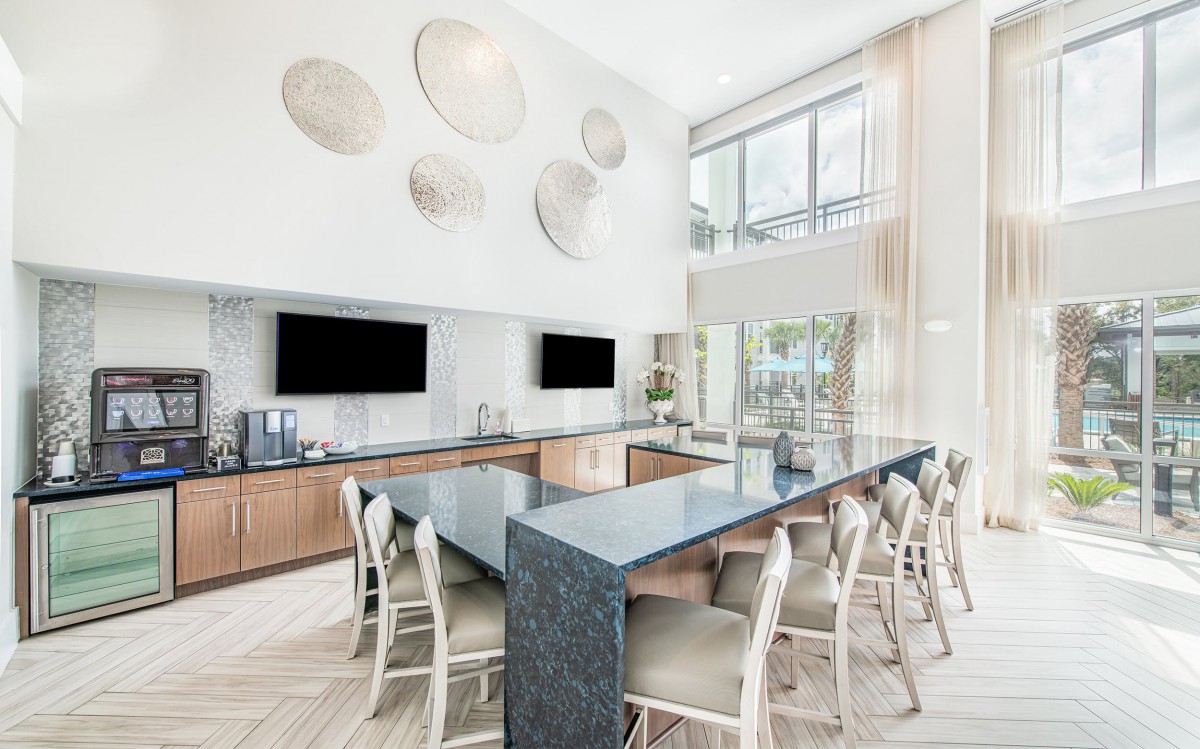 A modern kitchen with a large island and bar stools, featuring decorative wall art and multiple televisions.