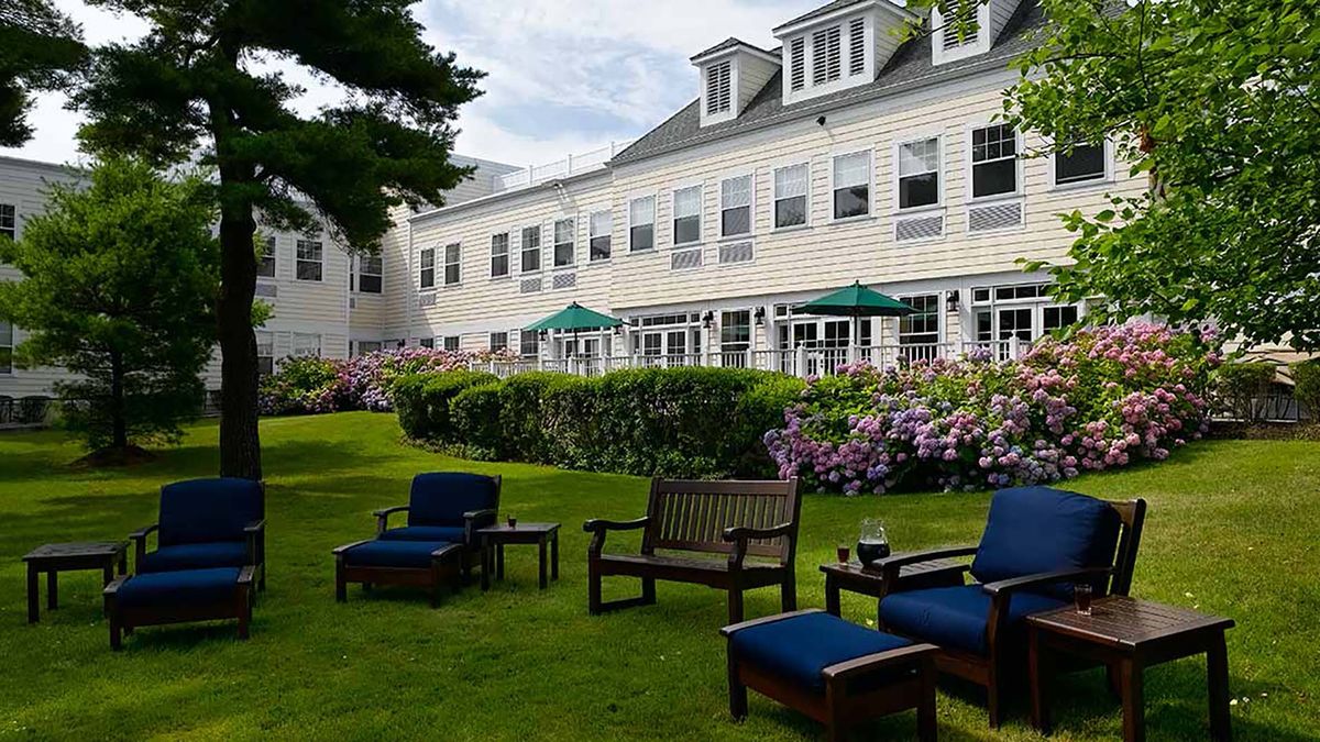 A charming garden area with outdoor seating and a backdrop of a large house.