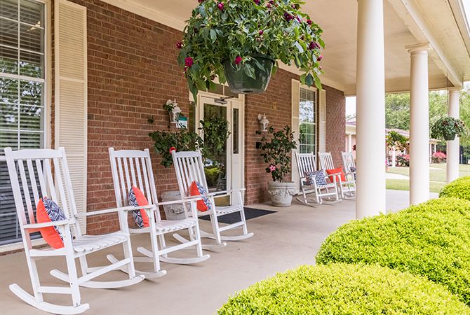 A charming porch with white rocking chairs and lush greenery.