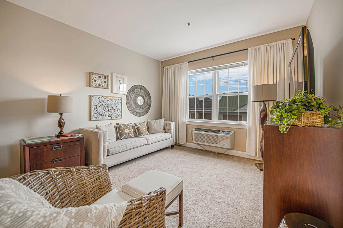 A cozy and elegantly decorated living room with a sofa, artwork, and natural light streaming through a large window.