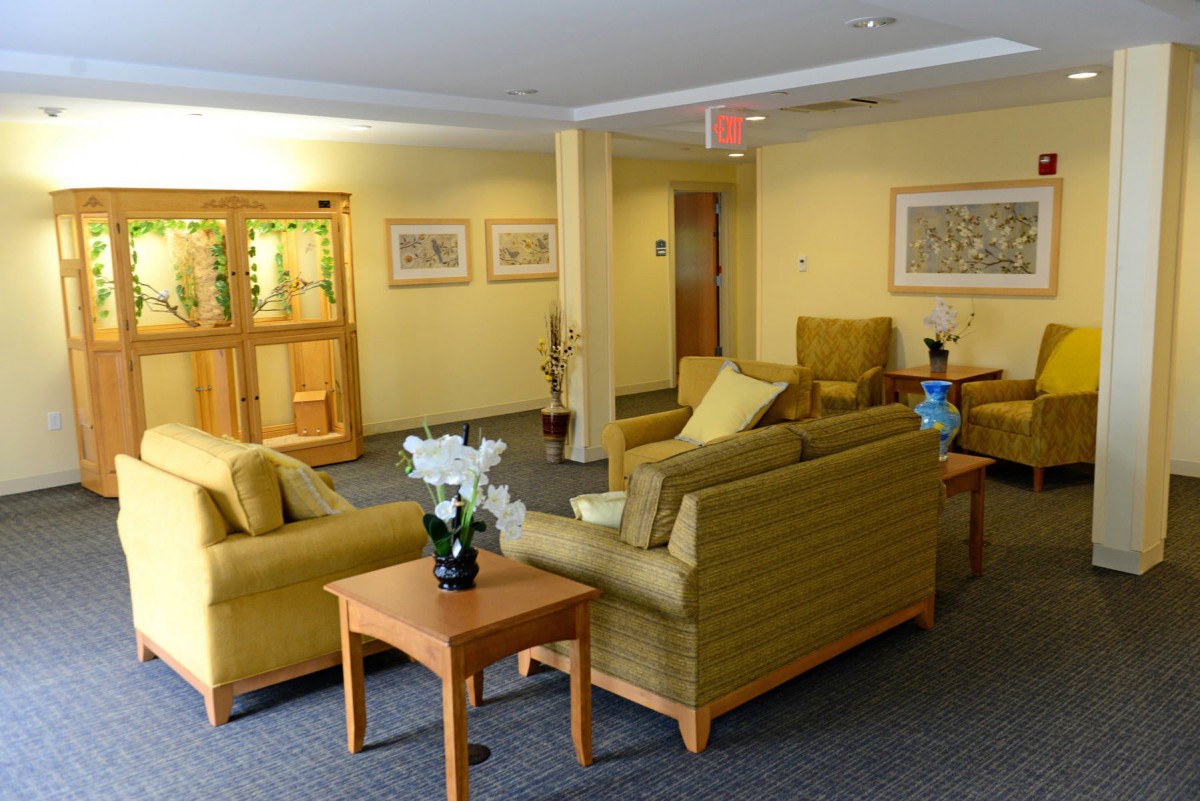 A cozy waiting room with yellow sofas, a wooden table, and framed artwork on the walls.