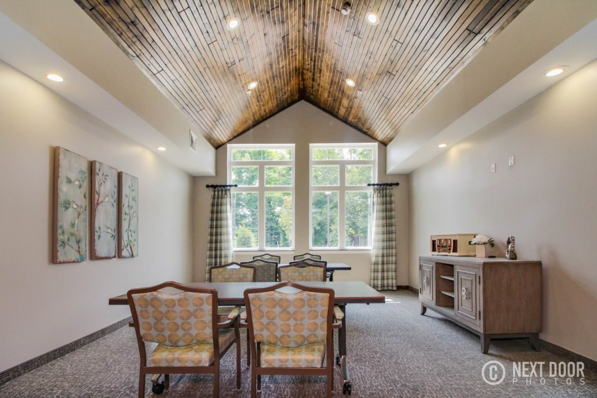 A spacious dining room with a wooden vaulted ceiling, modern furniture, and large windows allowing ample natural light.