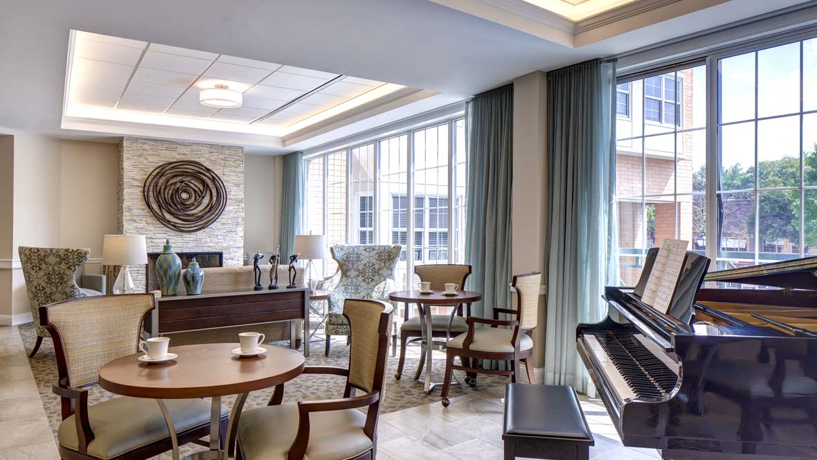 A cozy lounge area with elegant furniture and a piano, bathed in natural light from large windows.