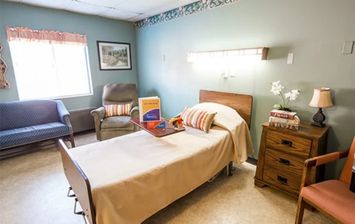 A neatly arranged hospital room with a single bed, chair, and window, providing a comfortable environment.