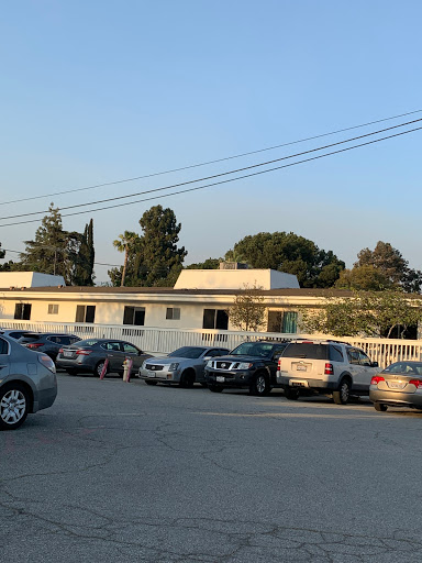 A view of a parking lot filled with cars, adjacent to a building, with trees and clear skies in the background.