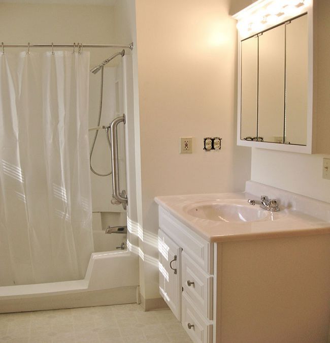 A bright bathroom featuring a sink with a mirror above, and a shower with a curtain.