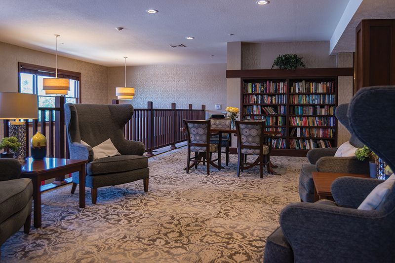 A cozy indoor library with a seating area, bookshelves, and a carpeted floor.