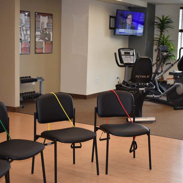 A fitness room with chairs fitted with resistance bands, a television, and exercise equipment.