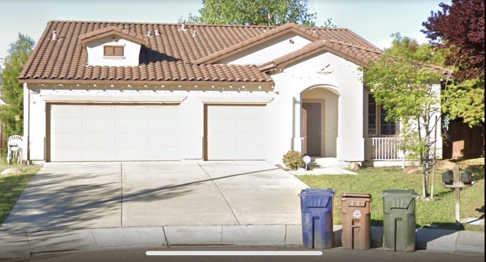 A suburban house with a three-car garage, driveway, and trash bins in front.