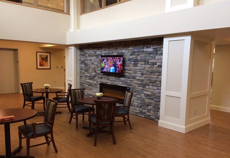 A cozy lobby area features a stone fireplace, a mounted television, and seating arrangements with tables and chairs.