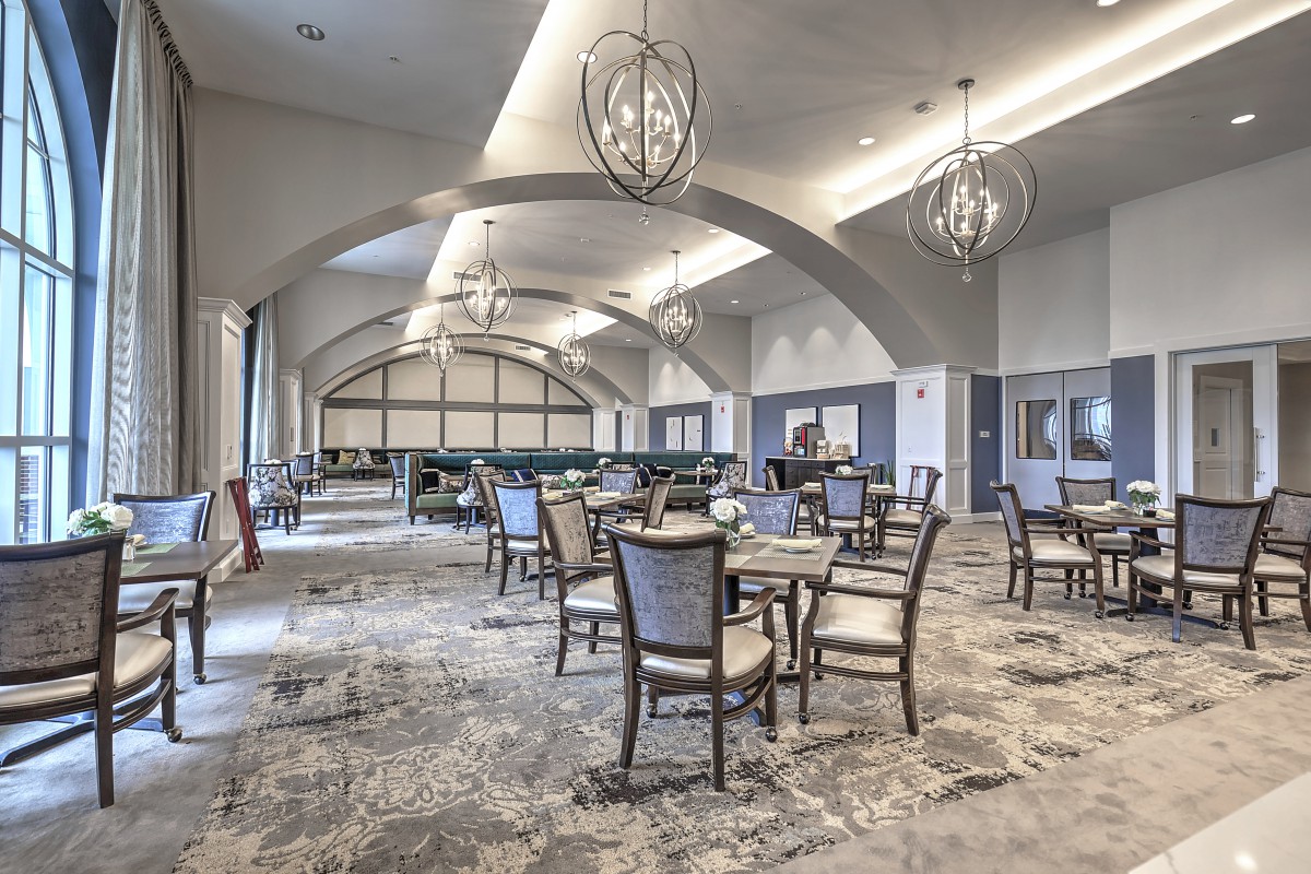 A spacious and elegantly designed dining area featuring modern chandeliers, arched ceilings, and stylish furniture.