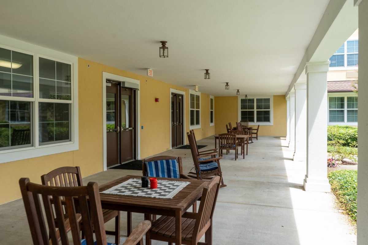 A covered patio with wooden tables and chairs arranged for outdoor seating against yellow walls.