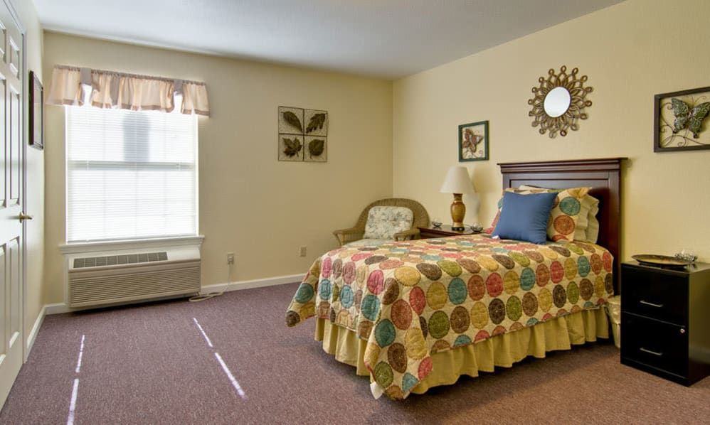 A cozy bedroom with a colorful quilt on the bed, art on the walls, and natural light from a window.