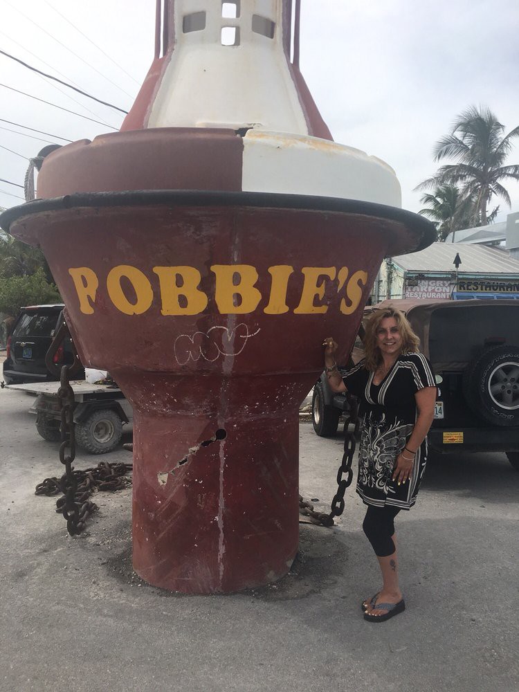 A person stands next to a large buoy marked 'BOBBIE'S' at a tourist attraction.