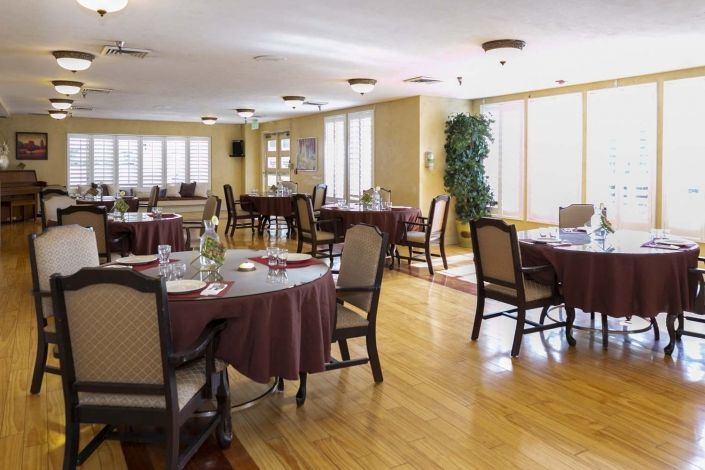 A well-lit dining area with round tables and upholstered chairs on a wooden floor.