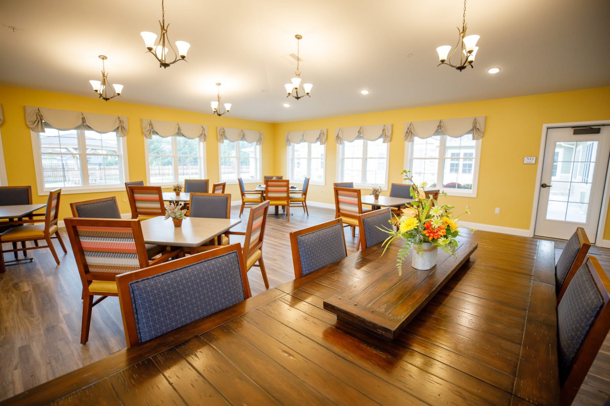 A spacious dining area with wooden floors, colorful chairs, and abundant natural light.